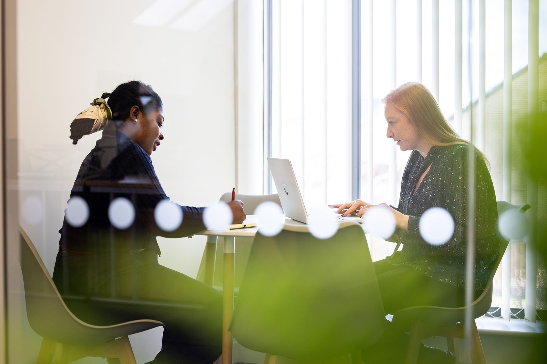 Two women sat at a desk working on laptops.